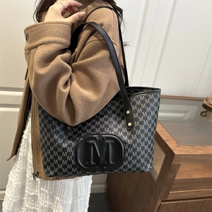 Detail view of stylish tote bag with 'M' pattern print and gold rivets on a chic model