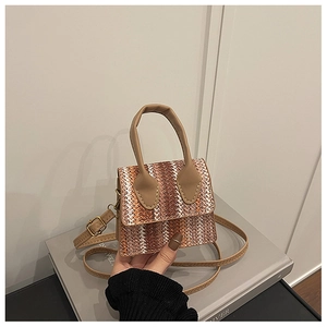 Detail of a mini straw woven crossbody bag with brown leather handles and hardware
