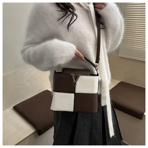 Brown and white leather crossbody bag with V-shaped buckle worn with a white knit sweater