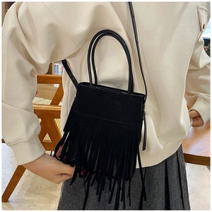 Close-up of black fringe bucket bag with long tassels and adjustable strap on a shoulder