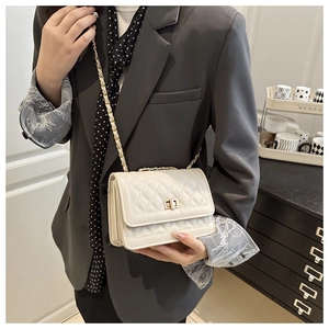 Detail of white quilted crossbody bag with golden twist lock and chain strap on model