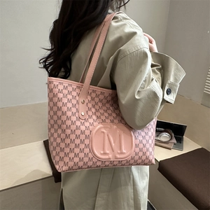 Detail of pink monogram PU tote bag with large M logo carried by a model in beige coat