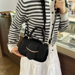 Detail of black crossbody bag featuring textured woven flap and gold metallic buckle