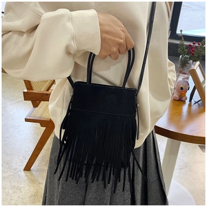 Detail of black bohemian tassel bucket bag with suede texture and long fringe accents
