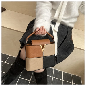 Detail of color-block tote bag with lychee texture and golden V-shaped metal buckle
