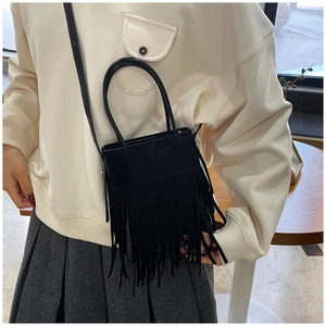 Detail of a black bohemian bucket bag featuring long fringe and a slim shoulder strap