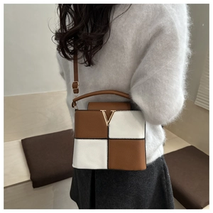 Detail of color-block bucket bag featuring golden V-clasp on soft brown and white leather