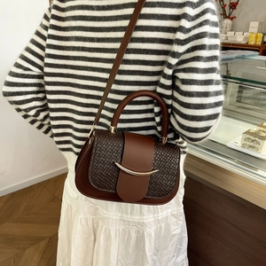 Detail of dark brown saddle bag featuring woven texture and golden crescent buckle