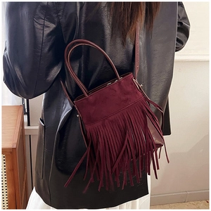 Close-up of a burgundy suede bucket bag featuring long vintage fringes and top handle