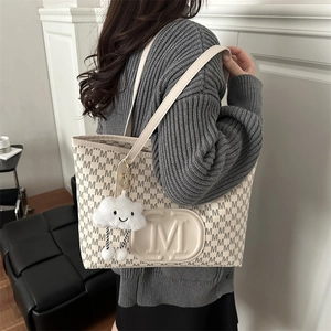 Detail of beige monogram tote bag with embossed M logo and cute cloud charm accessory