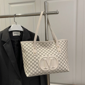 Detail of cream tote bag with M-pattern print and embossed central oval logo detail