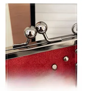 Macro detail of red suede bag with silver spherical lock and polished rivet studs
