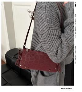 Close-up of burgundy leopard print shoulder bag with silver rivets and bow detail