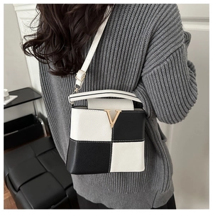 Detail of color-block crossbody bag with lychee texture and golden V logo on gray sweater