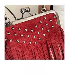 Detail of red suede bag featuring metal clasp closure, silver rivets, and long tassels