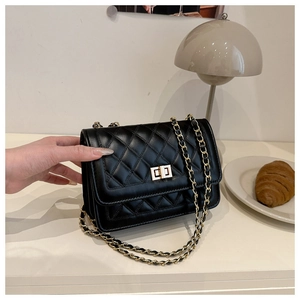Detailed view of black quilted crossbody bag with gold chain and metal lock on a table