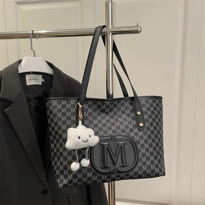 Close-up of black PU tote bag with M letter monogram and plush cloud charm accessory
