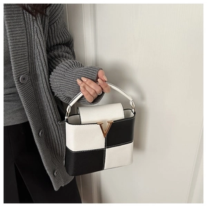 Detail of a chic black and white contrast leather handbag with a gold V-shaped metal buckle