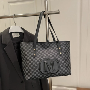 Detail of grey M-letter monogram pattern and embossed black oval logo on PU tote bag