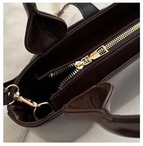 Close-up of smooth gold zipper and metallic hardware on deep brown leather tote bag