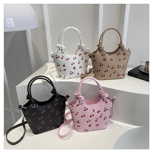 Detail view of cherry print bucket bags in white, tan, black, and pink with knotted handles
