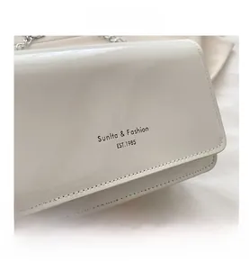 Détail du sac en cuir verni blanc cassé avec chaîne argentée et logo noir imprimé