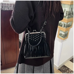 Detail view of black rivet shoulder bag with fringes and retro clasp worn by model