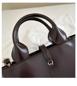 Detail of soft leather handles and golden spherical pendant on dark brown tote bag