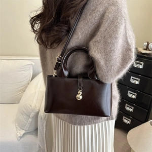 Deep brown leather bucket tote bag with gold metal charm shown from a side-view angle