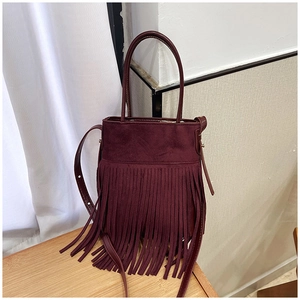 Detail view of burgundy suede bucket bag with long fringe tassels on wood surface