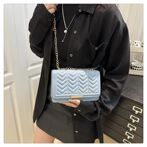 Détail du sac bandoulière bleu clair matelassé en V avec chaîne dorée porté par un mannequin