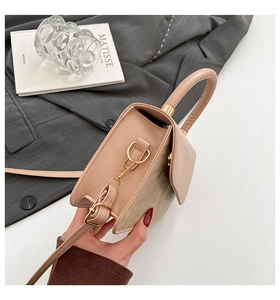 Detail der beigen Umhängetasche aus Leder mit goldener Hardware auf einem dunklen Anzug