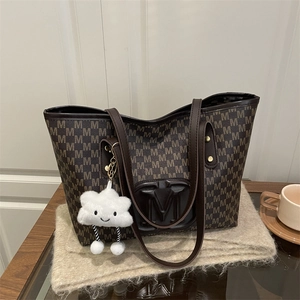 Detail of PU leather tote bag with M-pattern and plush cloud charm on a cozy surface