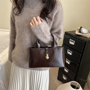 Detail of a dark brown glossy leather tote bag with unique golden gourd metal accessory