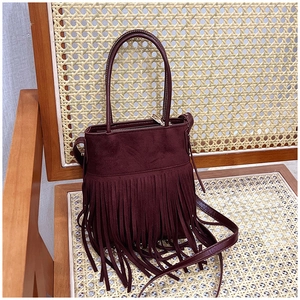 Detail of burgundy suede bucket bag with long fringes and strap on a vintage rattan chair