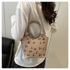 Detail view of cream bucket bag with cherry prints shown being worn by a model