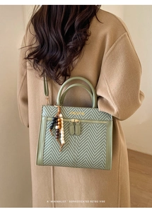 Details der grünen Retro-Handtasche mit Webstruktur, Goldlogo und Perlenanhänger