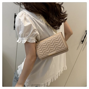 Détail du sac matelassé beige avec chaîne dorée porté à l'épaule par un mannequin