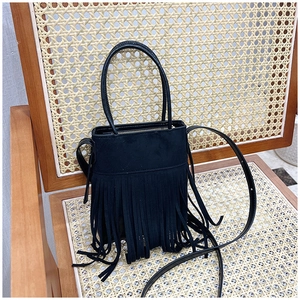 Detail of bohemian black suede bucket bag with long fringe on a wicker chair