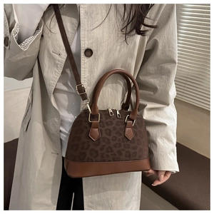 Brown leopard print shell bag shown as a crossbody with adjustable leather strap