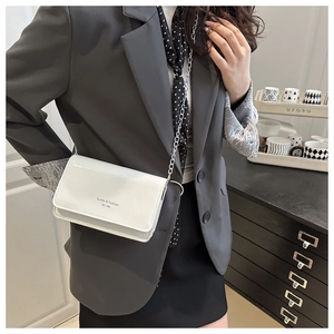 Sac bandoulière blanc avec logo noir porté par un mannequin en costume élégant