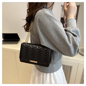 Détail d'un sac bandoulière noir matelassé avec surpiqûres en V et chaîne en métal doré
