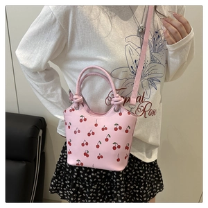 Fashionable pink bucket bag with red cherry print featuring top handles and shoulder strap