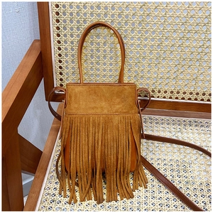 Detail of bohemian brown suede fringe handbag with round handles on a vintage wooden chair