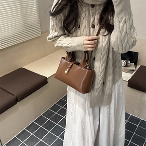 Detailed close-up of a brown leather bucket bag with gold hardware on a beige sweater