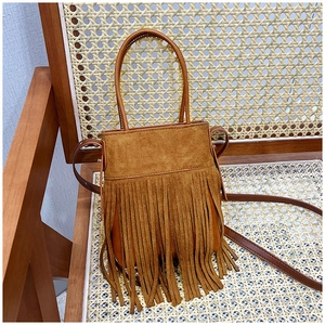 Detailed view of a brown suede bucket bag with long tassels on a vintage wooden chair