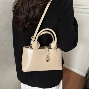 Close-up of beige glossy patent leather bucket bag with gold spherical charm detail