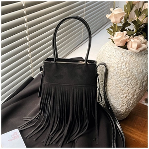 Detail of bohemian black suede handbag featuring long fringe tassels and leather handles