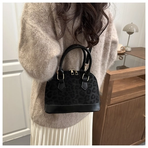 Detail view of black leopard print shell bag with golden hardware and leather straps