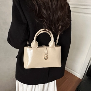 Beige patent leather bucket bag with gold charms shown as a crossbody on a model back view